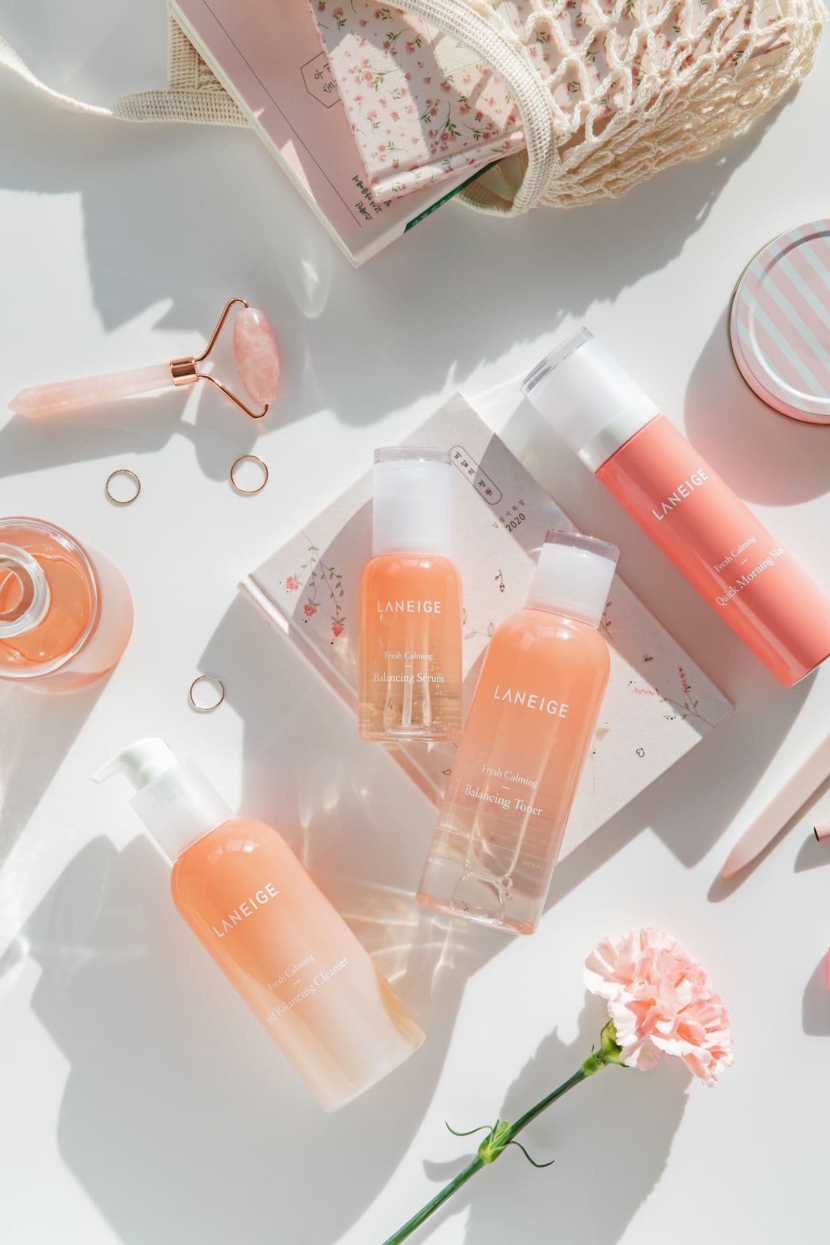 Soft pink skincare products arranged with a carnation flower