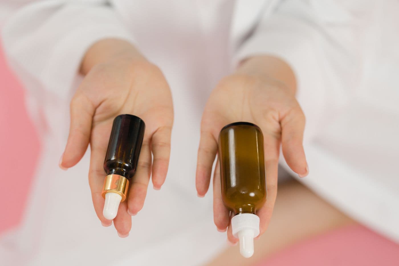 Hands holding two skincare serum bottles on a soft pink background